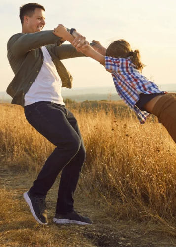 Nevető apa pörgeti kislányát egy napsütötte, aranyló mezőn a szabadban. Családi boldogság, apa-lánya kapcsolat, játék a szabadban, kirándulás, természet, szabadidő, gondtalan gyermekkor.