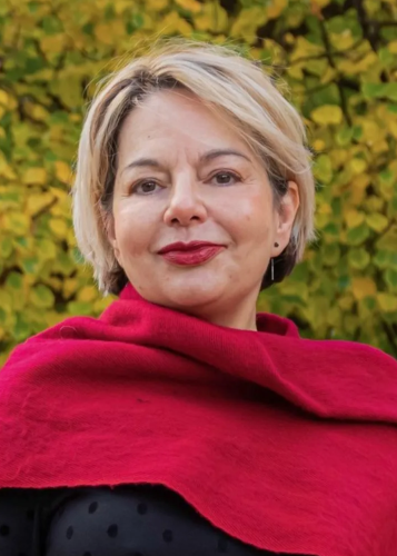 Közeli portré egy szőke nőről, aki bordó sálat visel, háttérben sárguló őszi levelekkel. Női portré, érett szépség, őszi hangulat, elegancia, szabadtéri fotózás, magabiztosság.