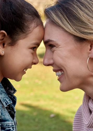 Közelkép egy nevető nőről és egy kislányról, akik a homlokukat egymásnak döntve mosolyognak a szabadban. Anya-lánya kapcsolat, szeretet, családi boldogság, meghitt pillanat, nevetés, szabadtéri életmód, gondoskodás.