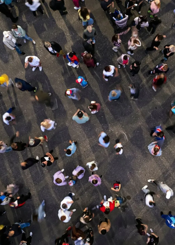 Madártávlati fotó egy aszfalton sétáló, színes ruhás tömegről. Városi élet, mobilitás, tömeg, gyalogosok, közösség, kitörés.